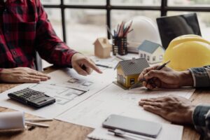 Engineer,Pointing,At,Building,On,Blueprint,And,Using,Laptop,To